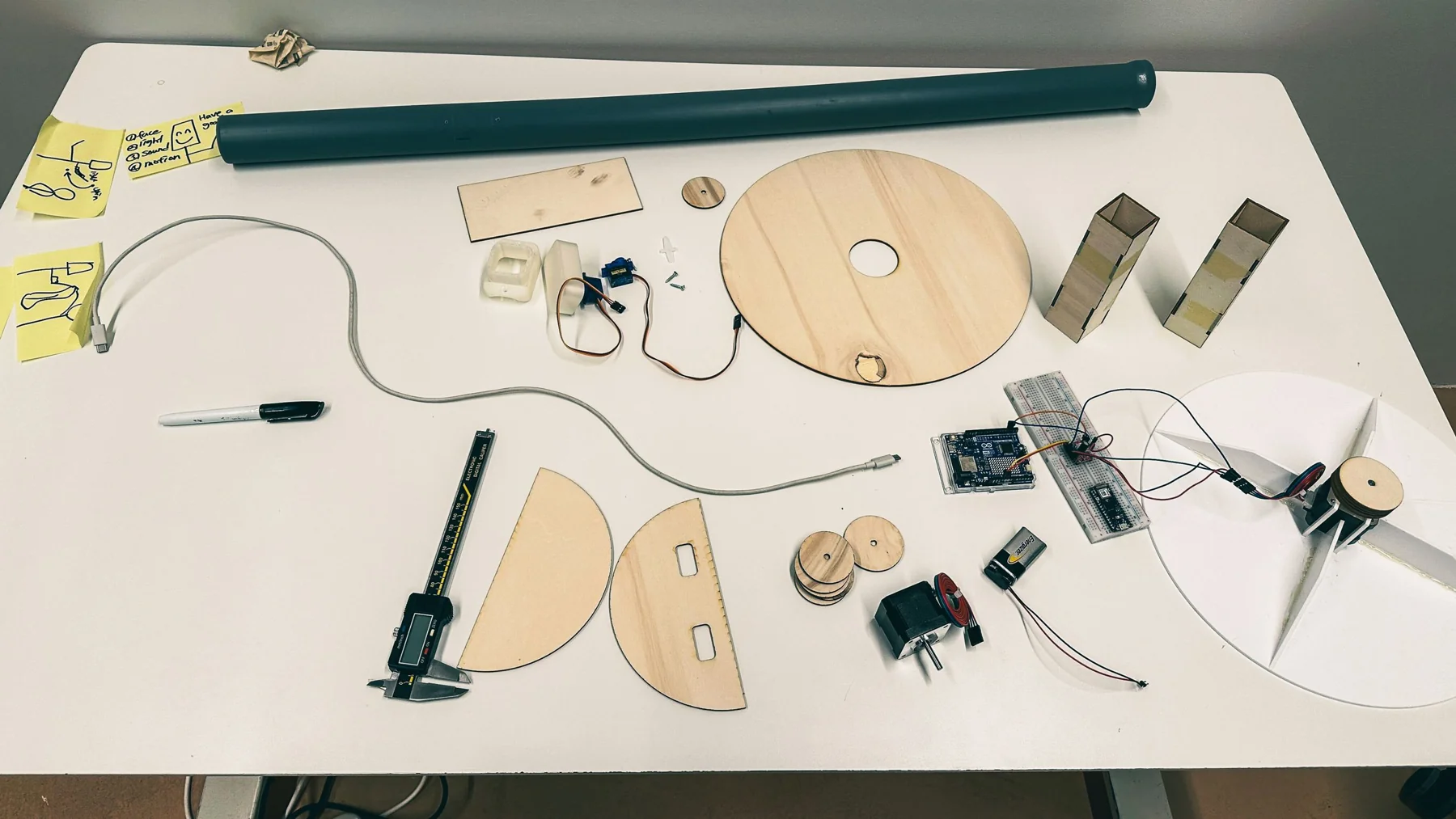 The parts laid out on a table: a pipe for the pole, laser-cut wooden pieces, a motor, a servo and an Arduino