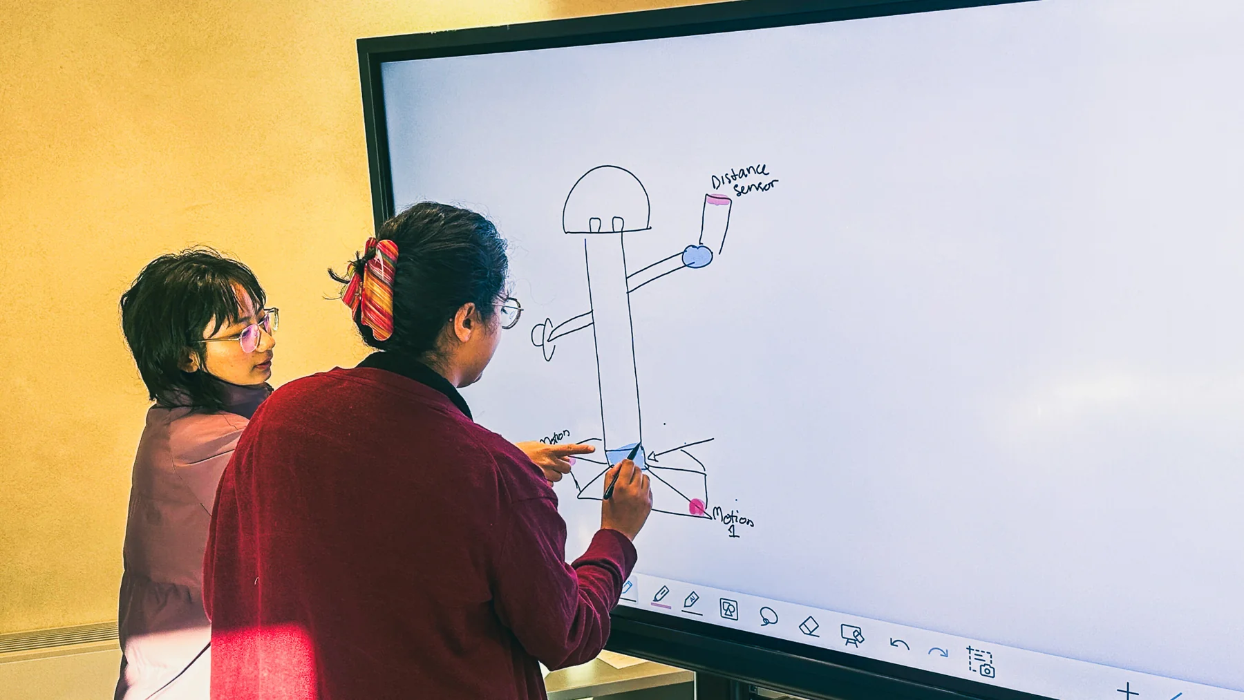 Two teammates sketching the coat rack on a digital whiteboard, marking the distance and motion sensors