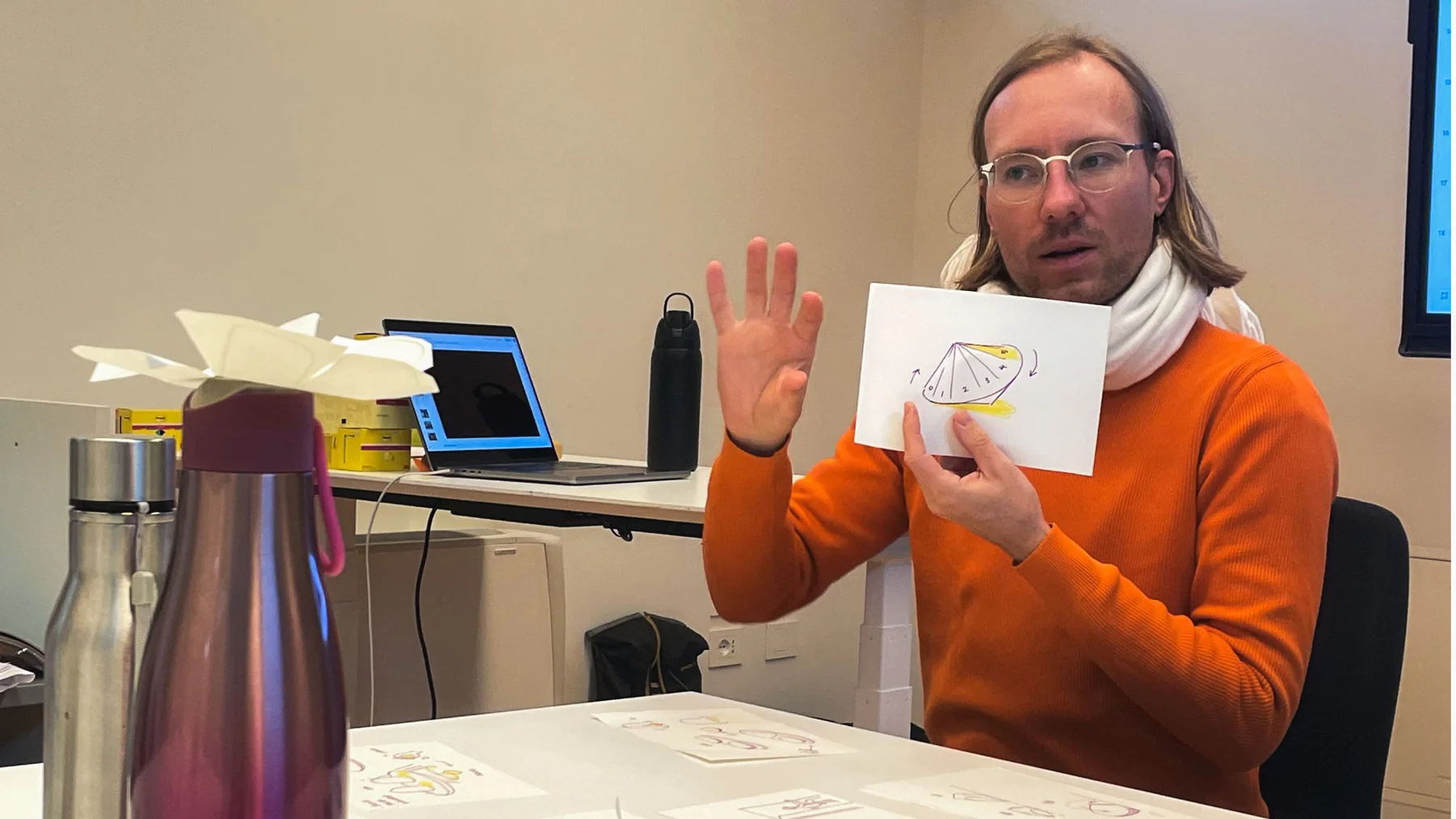 A teammate holding up a sketch of a dial while explaining an idea