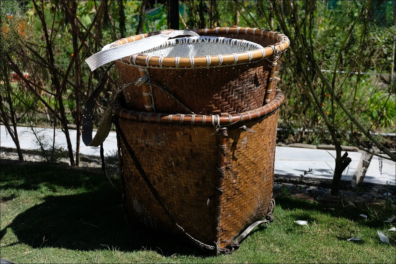 Two woven bamboo carrying baskets stacked on the grass in a garden in Ziro