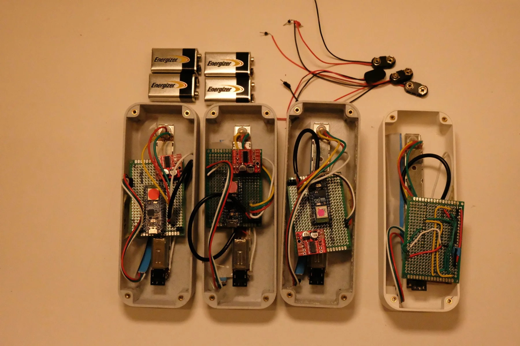 The four devices opened up to show their custom circuit boards, wiring and faders, with 9V batteries