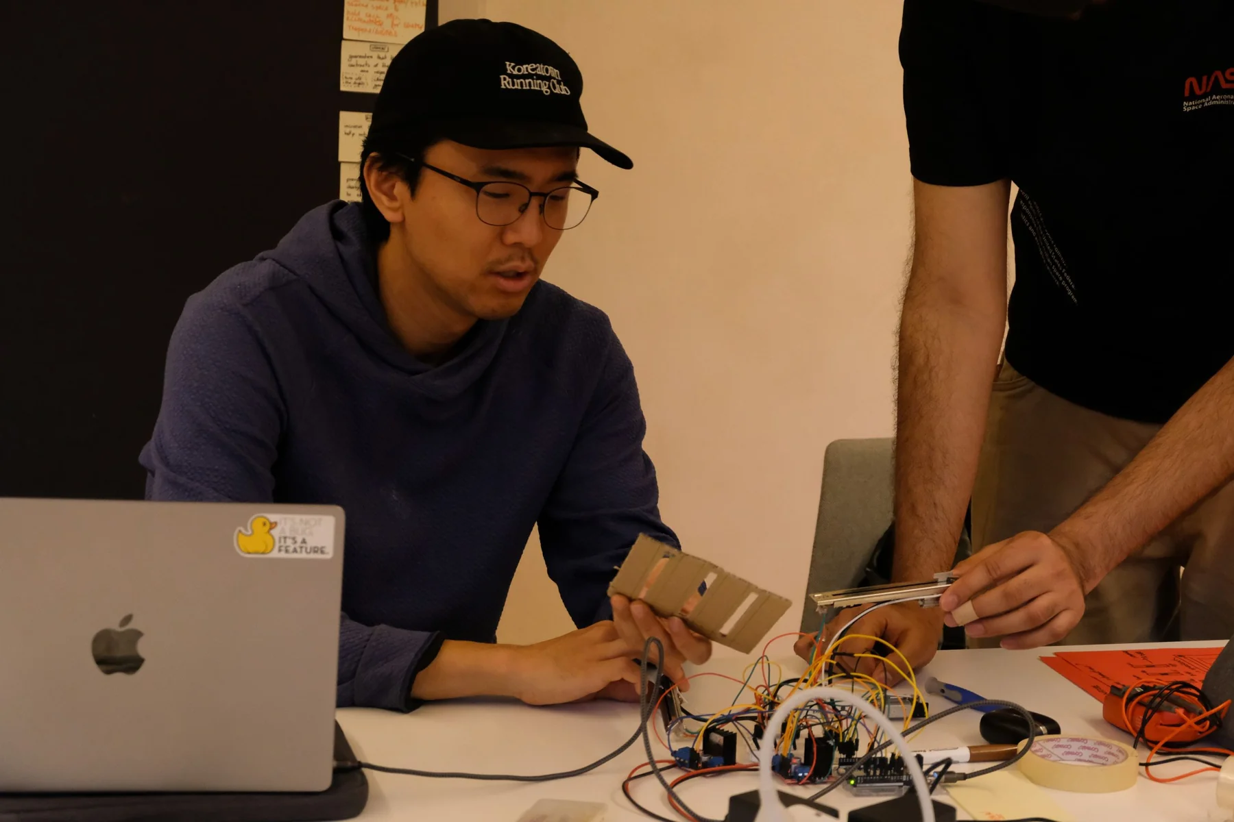 A teammate trying a cardboard fader mock-up beside the working electronics