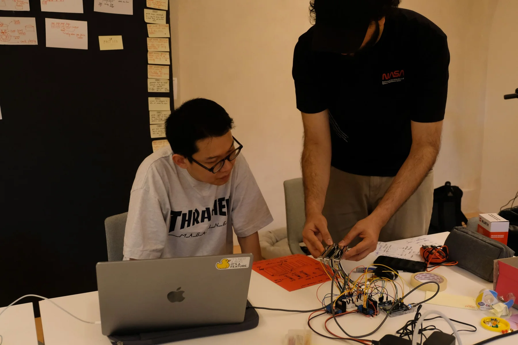 A teammate holding a set of faders over a breadboard full of wires while another watches the laptop